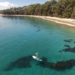 Person standing up on a SUP board paddling along a beach